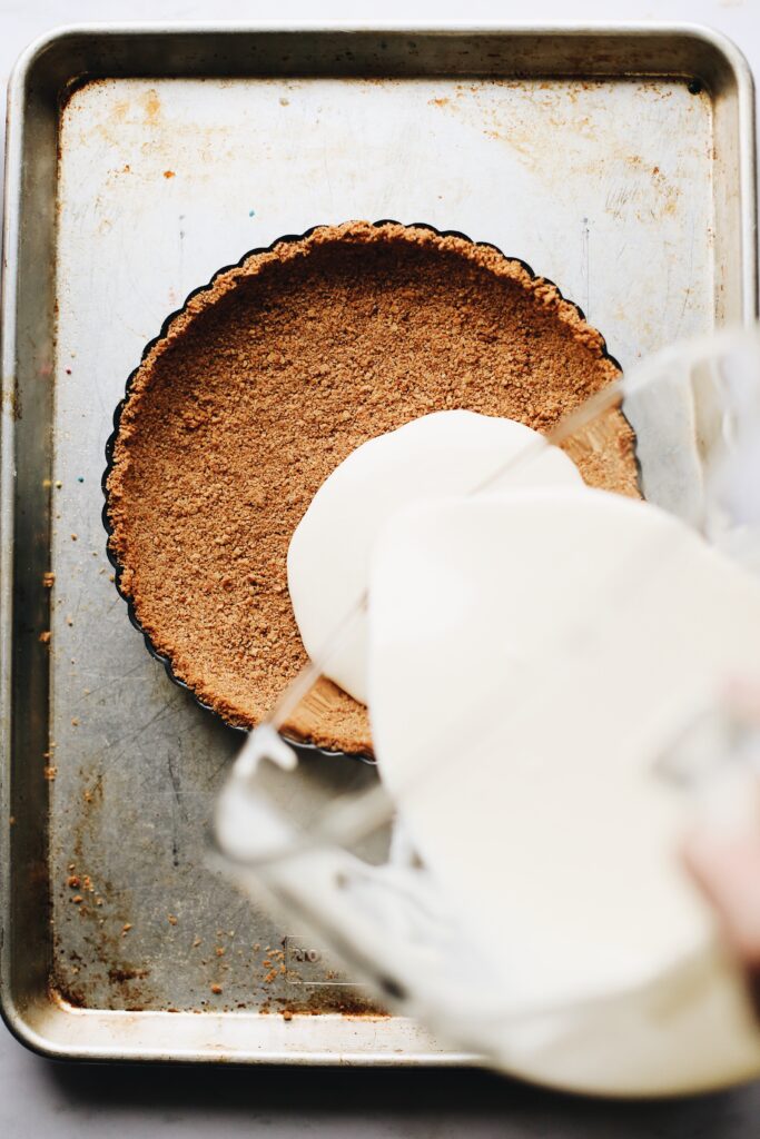 cheesecake filling being poured into a baked graham cracker crust